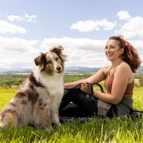 Dog and woman siting in the grass on a partly cloudy day