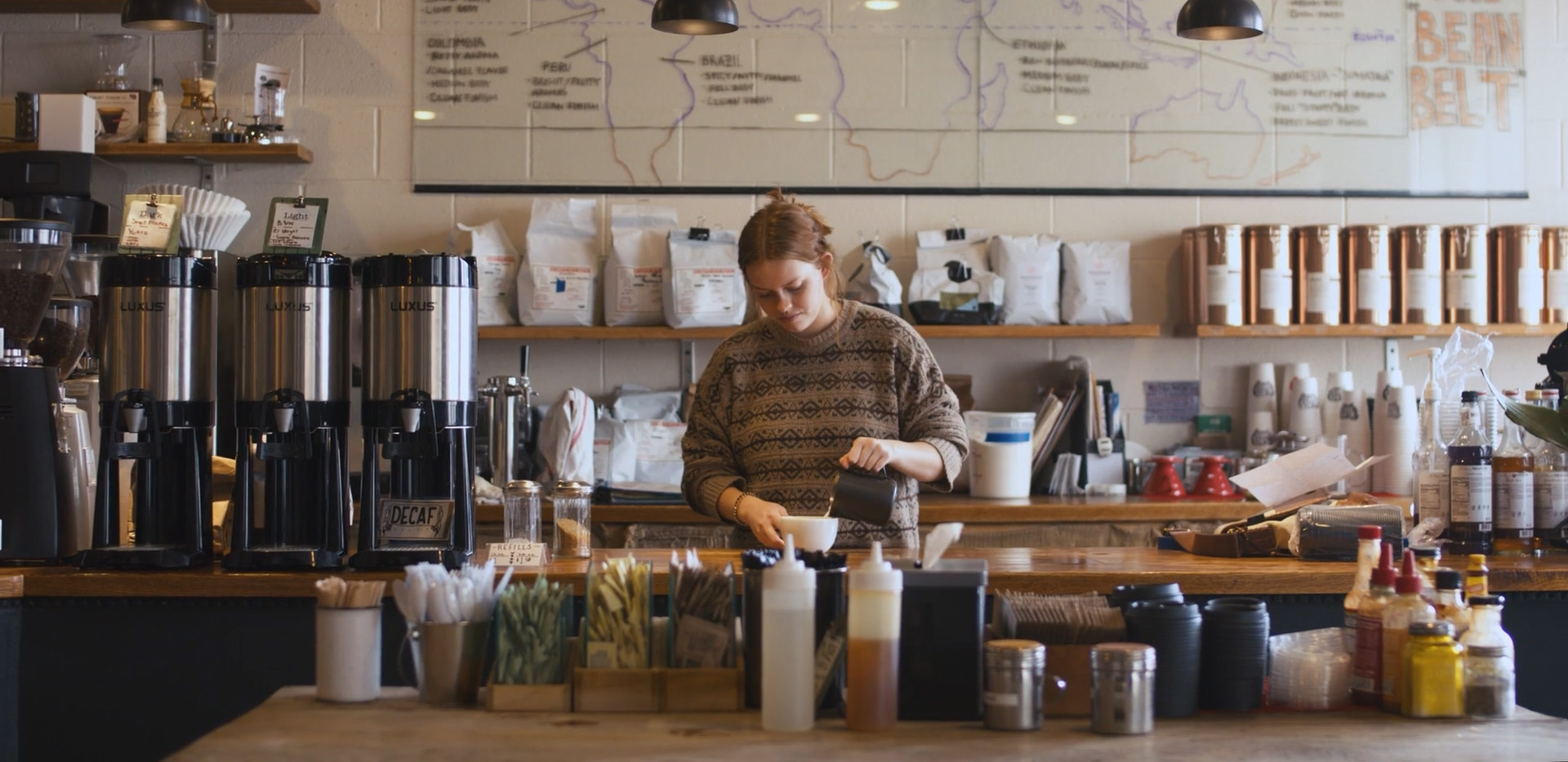 Woman working in a coffee shop pouring coffee into a mug
