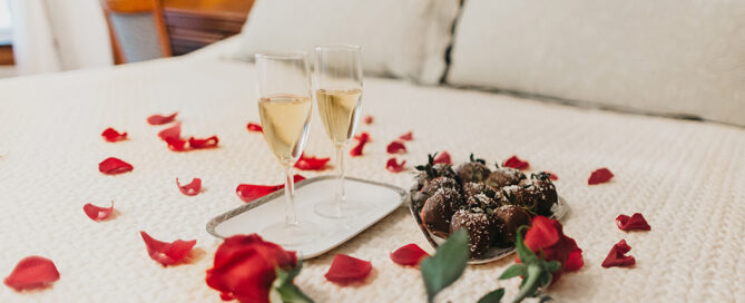 Rose pedals, champagne, and chocolate laid out on a bed