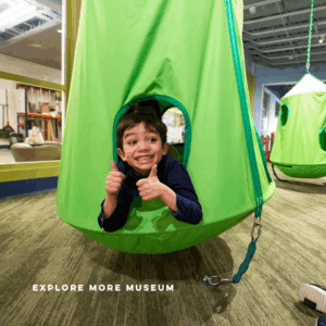 Child in green, hanging pod giving two thumps up and smiling.
