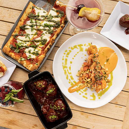 a table full of food from flat bread to meatballs and a cocktail
