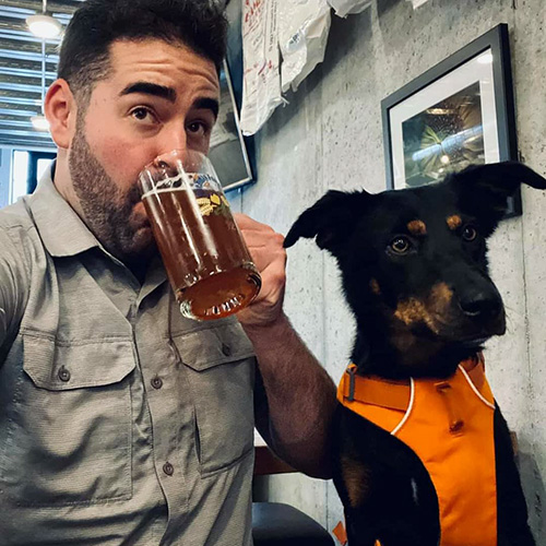 Man drinking a beer with his dog sitting next to him