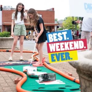 Two young girls playing putt putt in the street during Best Weekend Ever.